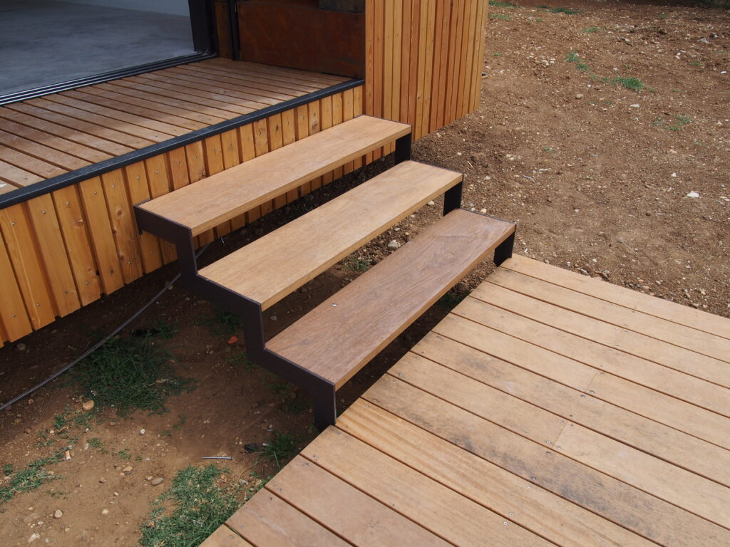 Escalier extérieur en bois avec structure métallique, reliant la terrasse à la maison en ossature bois bardée de mélèze et corten.